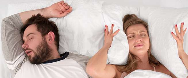 أمرأة تنام بجوار زوجها وتقوم بلف الوسادة حول إذنايها لتفادي صوت شخيره